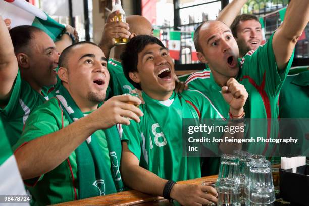 cheering men watching television in sports bar - beer bottle mouth stock-fotos und bilder