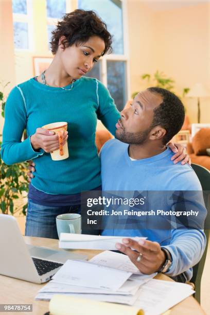 african american husband paying bills as wife watches - jon feingersh stock pictures, royalty-free photos & images