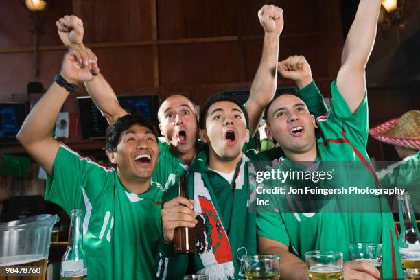 cheering men watching television in sports bar - beer bottle mouth stock-fotos und bilder