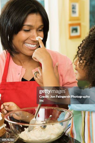 african american daughter putting icing on mother's nose - jon feingersh stock pictures, royalty-free photos & images