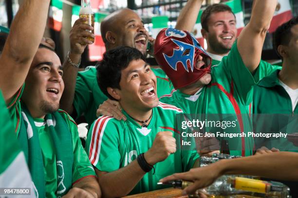 cheering men watching television in sports bar - beer bottle mouth stock-fotos und bilder