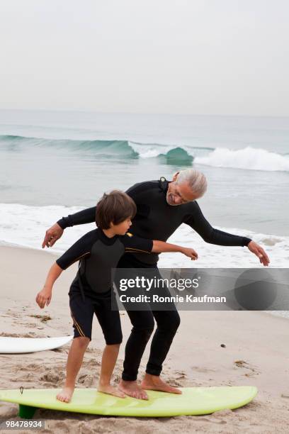 hispanic grandfather teaching grandson to surf - active seniors surfing stock pictures, royalty-free photos & images