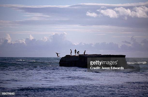teenage boys leap from a steep rock rising from the bass strait sea. - bass strait stockfoto's en -beelden