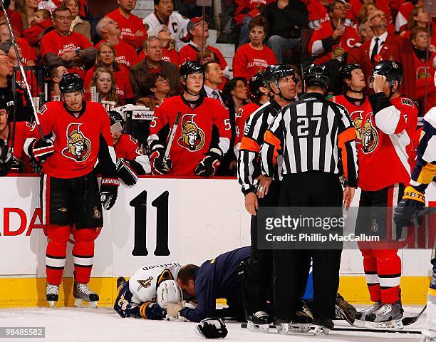 Milan Michalek and Brian Lee of the Ottawa Senators look on as a trainer attends to Drew Stafford of the Buffalo Sabres during a break in their NHL...