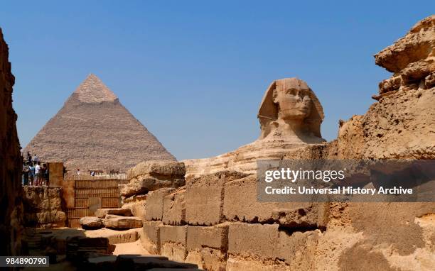 The Great Sphinx of Giza set against the Pyramid of Khufu. Limestone statue of a reclining sphinx. A mythical creature with the body of a lion and...