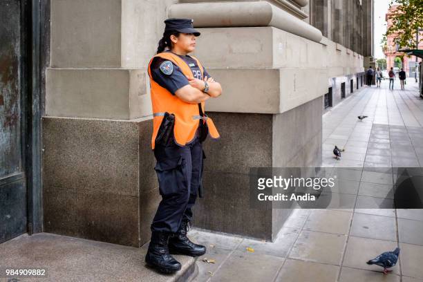Argentina, Buenos Aires. A policewoman in guard in front of the headquarters of the Banco de la NaciÌ_n Argentina , May Square . Some pigeons at her...
