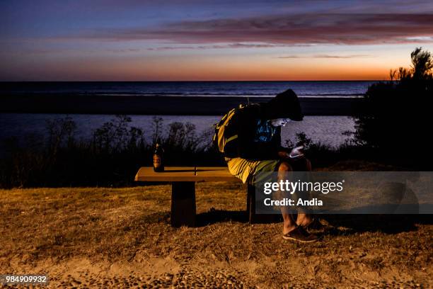 Uruguay, La Floresta, small city and resort on the Costa de Oro . At dusk, a young boy is seated on a bench, facing the Rio de la Plata, with a beer...