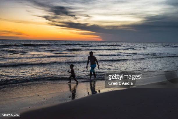 Uruguay, La Floresta, small city and resort on the Costa de Oro . At dusk, a young father and his son are running in the waves, on the shore.