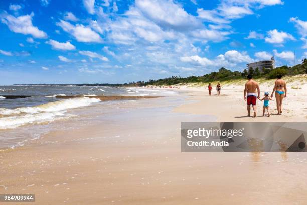 Uruguay, La Floresta, small city and resort on the Costa de Oro . A young couple is holding their daughter's hand, walking on a fine sandy beach.