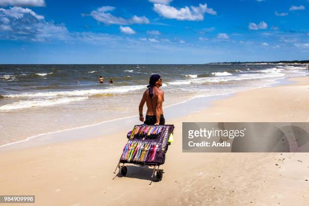 Uruguay, La Floresta, small city and resort on the Costa de Oro . A hawker selling necklaces and bangles is walking on the beach with his movable...