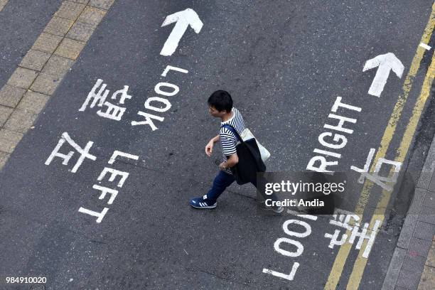 Hong Kong. Pedestrian crossing a street outside the crosswalks, with road marking in English and Chinese: 'Look right, look left'.