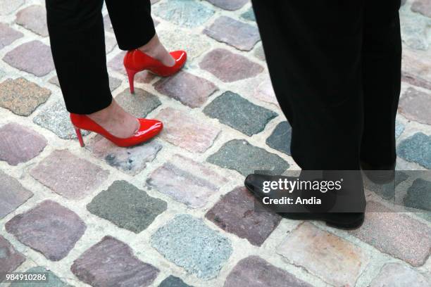 Close-up shot of the feet of a woman wearing red stilettos and feet of a man wearing smart shoes.