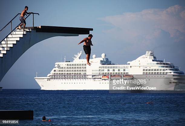Fat kid is jumping from a diving platform into the aegean sea while a cruise ship is crossing on July 16, 2009 in Rhodes, Greece. Rhodes is the...