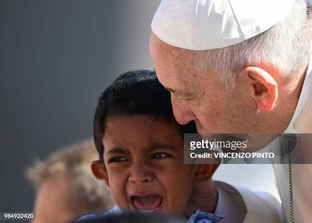 Pope Francis kisses a child as he arrives at the St. Peters square at the Vatican for his weekly general audience on June 27, 2018.