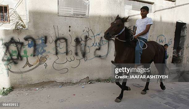 Palestinian youth rides a horse past graffiti allegedly sprayed by Jewish settlers on a wall in the Palestinian village of Jinsafut, which is located...