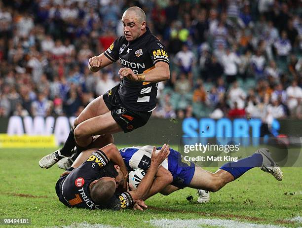 Bryson Goodwin of the Bulldogs is tackled by Beau Ryan of the Tigers as Liam Fulton jumps over the top during the round six NRL match between the...