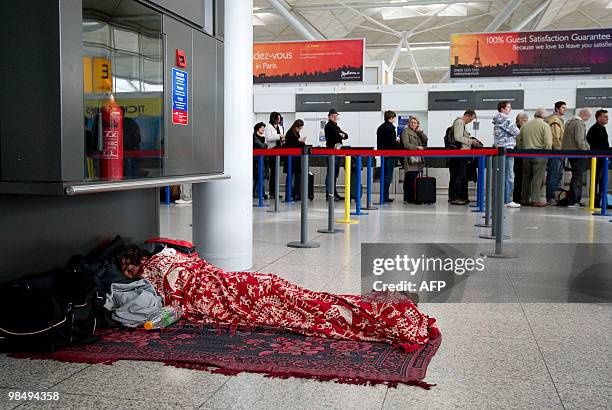 Man sleeps as other passengers queue at Stansted Airport in Essex, eastern England on April 16, 2010. A huge cloud of volcanic ash from Iceland cast...