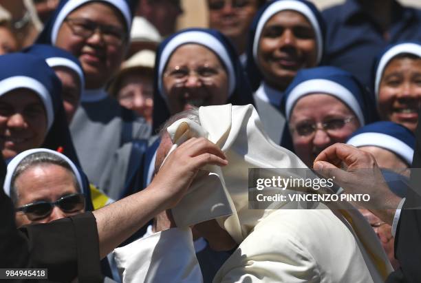 Pope Francis receives assistance as his mantle is lifted by gusts of wind, in St. Peters square at the Vatican at the end of his weekly general...
