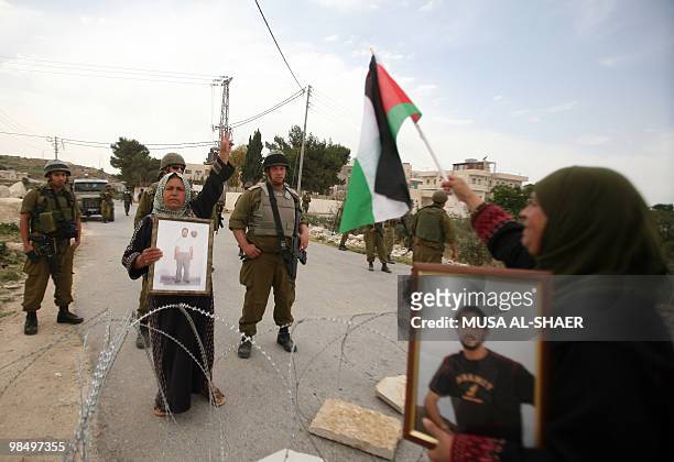 Israeli soldiers stand guard as Palestinian women hold pictures of their jailed relatives during a protest in the village of Maasrah, near Bethlehem,...