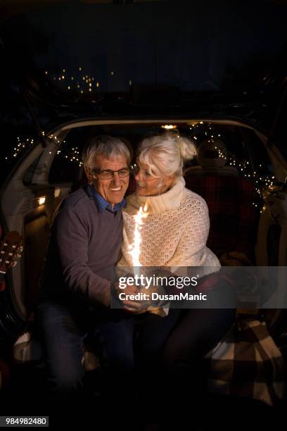 couple de personnes âgées s’asseoir dans le coffre de la voiture ouverte et tenir les bougies bâtons dans leurs mains - sasseoir photos et images de collection
