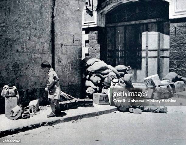 Photograph of an Arab soldier guarding a road block in the Old City in Jerusalem, whilst a young boy searches through the rubble. Dated 20th Century.