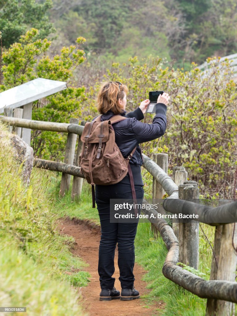 Woman walking and taking a picture with mobile phone in the fumaroles of a volcano of the Terceira Island, in the Azores islands, Portugal.