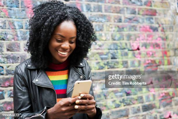 smiling woman using smart phone next to colourful wall. - bunter mantel stock-fotos und bilder