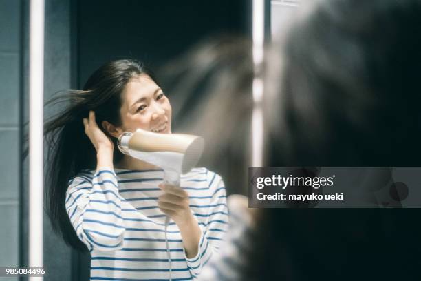 young woman who dries hair with a dryer - ヘアケア stock pictures, royalty-free photos & images