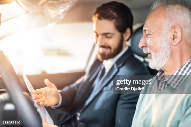 happy young car salesman talking with interested male senior customer. - car show ad stock pictures, royalty-free photos & images