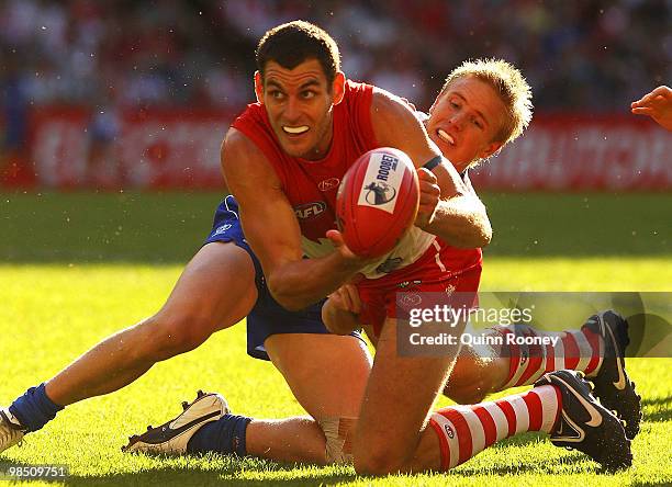 Mark Seaby of the Swans handballs whilst being tackled by Liam Anthony of the Kangaroos during the round four AFL match between the North Melbourne...
