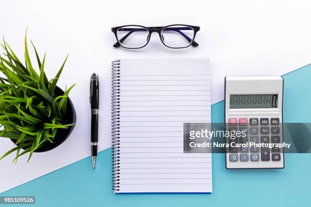 top view of note pad, calculator, pen, eyeglasses and green plant - office work flat lay stock-fotos und bilder