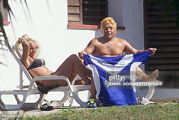 Argentine ex-soccer player Diego Armando Maradona holds a shirt of the Argentine soccer team Velez Sarsfield as he sits next to his wife Claudia...