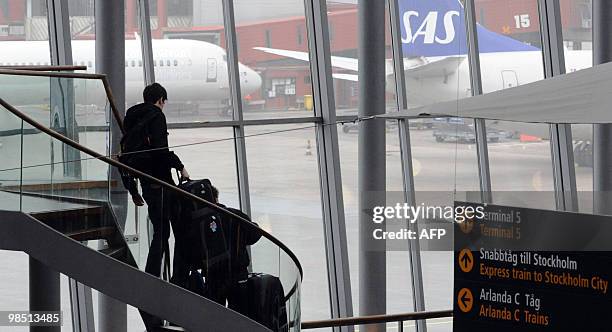 Passengers carry their luggages down a stairway in front of two Scandinavian Airlines aircrafts parked at Arlanda airport in Stockholm, on April 17,...