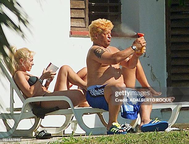 Former Argentine soccer star Diego Armando Maradona sprays a sun shield beside his wife Claudia Villafane 28 January 2000 in Havana where he is...