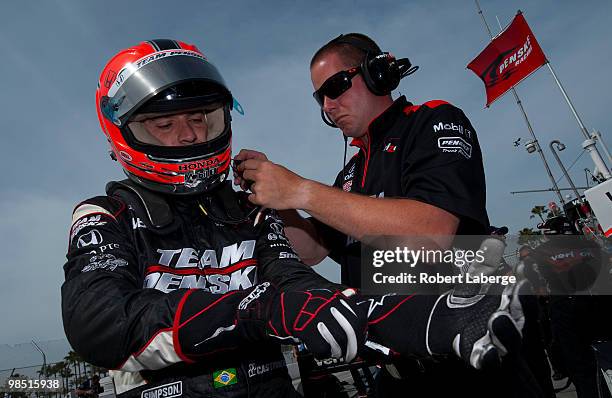 Helio Castroneves of Brazil, driver of the Team Penske Dallara Honda gets help from a crew member to put his helmet on before practice for the...