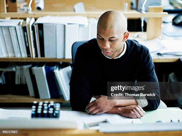 businessman seated at workstation studying plans - newbusiness stock pictures, royalty-free photos & images