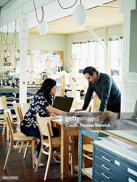 two coworkers examining documents at table - newbusiness stock pictures, royalty-free photos & images