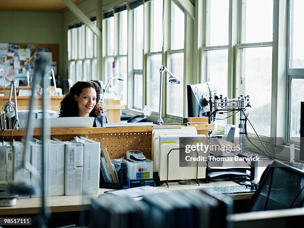 businesswoman seated at workstation smiling - newbusiness stock pictures, royalty-free photos & images