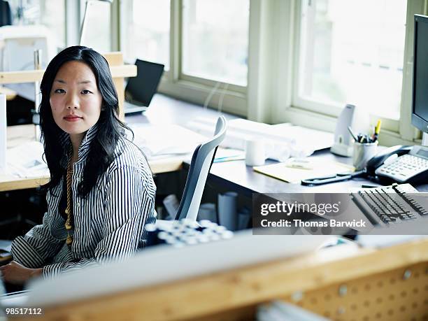 businesswoman seated at workstation in office - newbusiness stock pictures, royalty-free photos & images