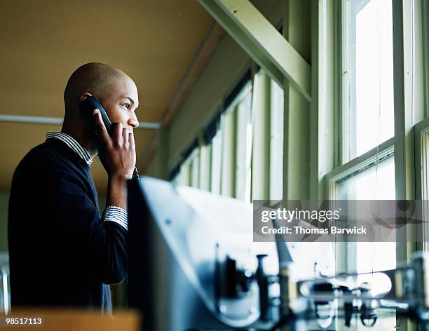 businessman on phone looking out window of office - newbusiness stock pictures, royalty-free photos & images