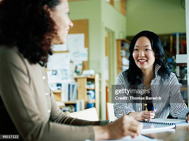 businesswomen seated at office table in discussion - newbusiness stock pictures, royalty-free photos & images