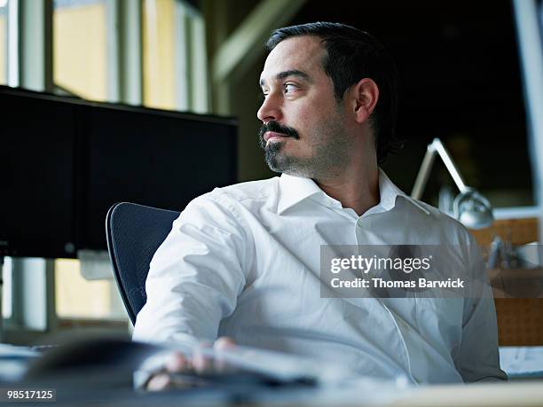 businessman seated at desk in office looking out - newbusiness stock pictures, royalty-free photos & images