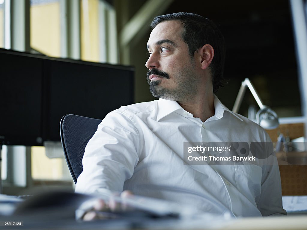 Businessman seated at desk in office looking out