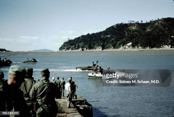 Army soldiers on a dock watch amphibious Marine Corps vehicles in the water, South Korea, October 1952.