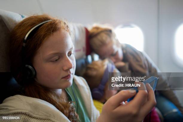 girl sitting on a plane using smartphone to spend time while waiting for landing - mother 2017 film stock pictures, royalty-free photos & images
