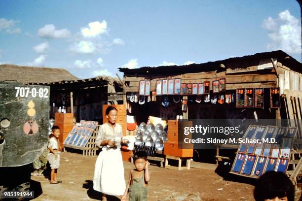 View of women, along with several children, as they walk past a photographer's stand on Potchon Road, South Korea, January 1952.