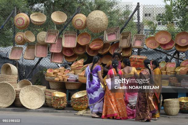 Indian customers bargain with a Yerukala tribal woman selling bamboo baskets on a roadside in Hyderabad on June 27, 2018. - Yerukalas are indigenous...