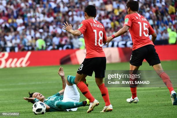 Germany's midfielder Mesut Ozil reacts after falling on the football pitch next to South Korea's midfielder Moon Seon-min and South Korea's...