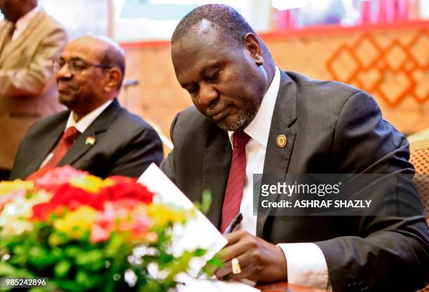 South Sudanese rebel leader Riek Machar signs documents as Sudanese President Omar al-Bashir is seated after the two South Sudanese arch-foes agreed...