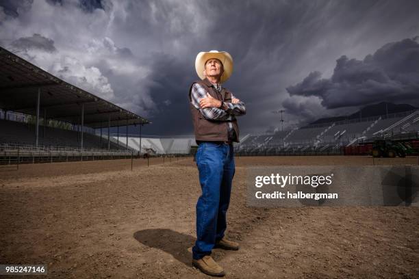 cowboy posing in rodeo arena under dramatic stormy sky - western storm stock pictures, royalty-free photos & images